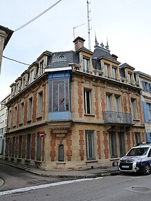 Bâtiment d'angle en pierre et briques rouges avec un oriel peint en bleu.