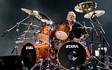 Short-haired man in a black shirt on a drum kit