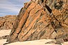 Outcrop of banded and folded metamorphic rock with snow patch in foreground