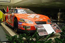 An orange race car with sponsors logos in a museum setting