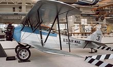 A blue-and-white biplane with "U.S. Air Mail" on the fuselage and "3" on the tail