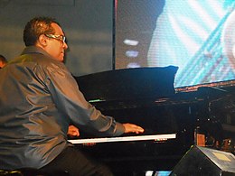 un homme avec des lunettes assis au piano sur scène