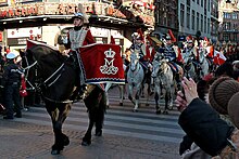 Des militaires danois à cheval, vêtus de rouge et de bleu, lors d'un défilé dans les rues, au milieu de la foule.