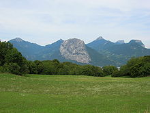 Montagne inclinée s'élevant par-delà une prairie, au-dessus d'une vallée, avec d'autres montagnes en arrière-plan.