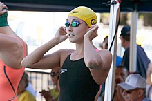 Rachel Bootsma im schwarzen Badeanzug bereitet sich auf das Rennen vor. Sie trägt bereits ihre Schwimmbrille und die gelbe Badekappe der University of California.