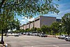 An angled view of a long, modern, stone building with seven bays, every other one being one story taller than the previous.