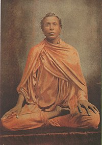 Sri Lankan man dressed in dark robes, sitting in meditation posture.