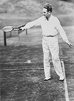 A man in a white clothing with a wooden tennis racket