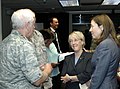 Two adult women talk with an older white-haired man in camouflage inside a dark room. (from Washington (state))