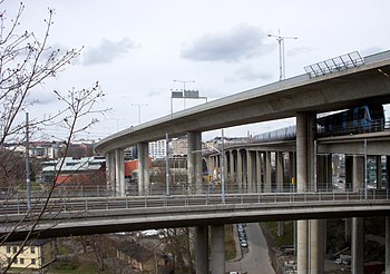 Skanstullsbron då och nu sedd från Skanskvarn. På bilden till vänster syns en av Stockholms äldre gröna tunnelbanevagnar och på bilden till höger kör den nya vagnen av typ C20 över bron. Sedan 1946 har bilden förändrats en hel del; 1984 invigdes ytterligare en högbro, Johanneshovsbron, och 2002 tillkom slutligen Fredriksdalsbron för Tvärbanan (som syns i förgrunden). På bilden från 1953 reser sig Åhléns Söders kända torn på Södermalms sida. Tornet och byggnaden finns kvar men döljs nu av Johanneshovsbrons höga spann. Byggnaden längst ner till vänster hör till Sundsta gård. Färgfotografiet från 1953 togs av Gustaf W. Cronquist.