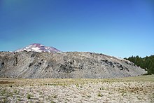 A rough-textured light-colored lava dome, with a volcanic peak behind