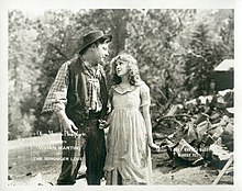 A young woman standing next to a tall strong country-side man.