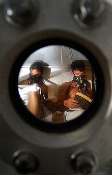 View through the viewing port of a large decompression chamber showing two divers relaxing while they decompress on oxygen using the built-in breathing system masks fitted inside the chamber.