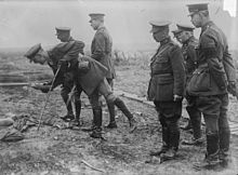 photographie du roi, portant un uniforme d'officier britannique, est entouré d'officiers dont l'un tient un obus à la main