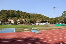 Photographie au niveau du sol d'une piste d'athlétisme rouge avec les tribunes au fond.