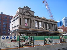 Dilapidated looking two storey building surrounded by a construction side with a crane behind.