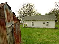 "A white, wooden house with a greenish roof in the middle of a green lawn."