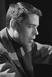 Photographie en noir et blanc de Jacques Brel jeune, cheveux courts, portant un pull sombre et une veste à chevrons.