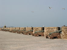 Vue par l’arrière d’une rangée de canons pointant à travers une muraille.