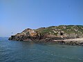 Mer calme, ciel bleu dégagé. Au centre de l'image, petite falaise s'enfonçant doucement dans la mer.