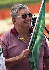 Donnie Allison wearing an unbuttoned T-shirt and holding a green flag with writing in his right hand