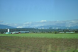 Farm fields, with South Slope, Burnaby, and the Metrotown skyline in the distance.