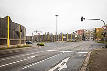 Foto einer großen Straßenkreuzung mit Ampel, Halteschildern und Richtungspfeilen auf zwei Fahrbahnen. Die Fahrbahnen sind teilweise mit Lärmschutzwänden begrenzt.