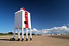 White wooden lighthouse with red vertical stripe, supported on nine legs