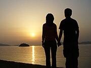 海辺で夕陽を眺めるカップル