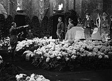 Photographie en noir et blanc de Hitler effectuant le salut nazi devant le cercueil de Heydrich, entouré de fleurs, le 9 juin 1942