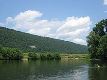 An image of a river in the foreground and a forested mountain ridge in the background, topped with a blue sky and clouds