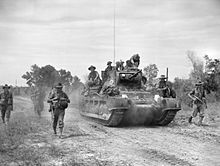 Soldiers advance along a road beside a tank