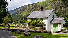 Photographie couleur du bureau d'information du parc national des montagnes de Wicklow à Glendalough, bâtiment d'aspect récent à la façade blanche et aux volets verts, dans un paysage lui-même verdoyant