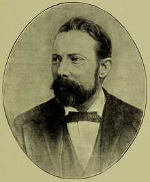 Image is an oval, black-and-white portrait of a distinguished man with a beard and bow tie