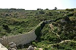 View of a valley with a fortified bridge cutting across it.