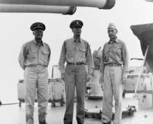 Black and white photograph of three men with caps standing on a ship's deck