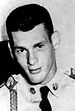 A young man in his in his military uniform looking forward towards the camera. He has a slight smile and his head is down and to the left.