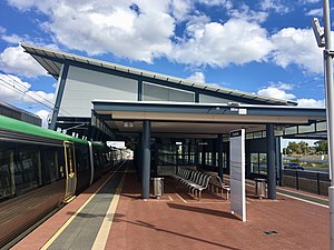 Brick platform with large metal shelter and a train stopped to the left