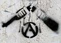 Das Symbol des zerbrochenen Gewehrs wird zuweilen mit dem anarchistischen A im Kreis verwendet und taucht gelegentlich als Stencil auf (abgebildetes Beispiel an einer Fassade in Frankreich, März 2011)