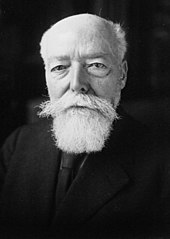 Photo en noir et blanc d’un homme chauve et à la barbe blanche posant de face