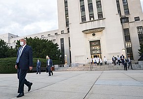 Trump, wearing a suit and face mask, walks out of Walter Reed Hospital, a 1939 classical revival building