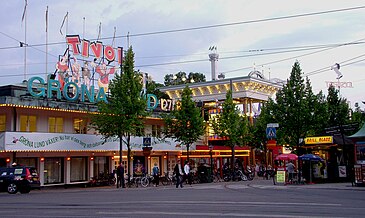 Ett besök på Gröna lund i juli 1963 och i juli 2010. Hörnhusen Djurgårdsvägen/Allmänna gränd ter sig ganska lika, med den stora, gröna texten "GRÖNA LUND" och ljuskedjorna längs takkanten. På taket har texten "TIVOLI" tillkommit. På bilden från 1963 görs reklam för uppträdanden av Evert Taube. På bilden från 2010 syns även Gröna Lunds nya, höga entrébaldakin, som är en kopia av originalet.