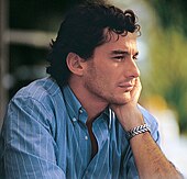 Photographic portrait of Ayrton Senna predominately showing the right side of his face with his left hand on the left hand side of his face and he is wearing a T-shirt