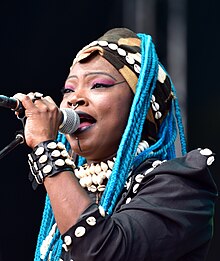 Oumou Sangaré wearing a patterned outfit, singing into a microphone onstage