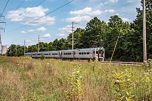 Silver single-level electric passenger train passing through grassand