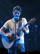 A man playing a guitar and singing on stage at a concert.