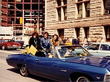 Three people sitting up on the back seat of a corvette, most likely participating in a parade or procession.