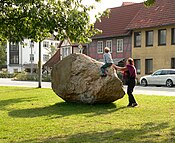 Findling mit Personen als Größenvergleich. An der linken Seite zu erkennen ist die Stelle, an der bei der Bergung ein Stück abgebrochen ist.