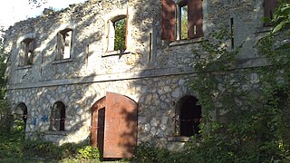 Façade d'une bâtiment à deux étages, en ruine, avec une grande porte métallique à deux battants.