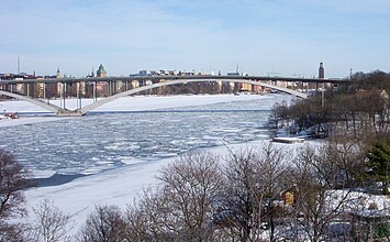 En vy från Långholmen över Riddarfjärden mot öst med Stockholms rådhus och Stockholms stadshus i bakgrunden. I november 1935 förändrades stadslandskapet när Västerbron invigdes. Fotografiet från 1926 är taget av Gustaf W. Cronquist på en autochromplåt.